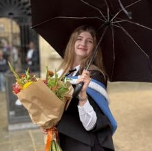 Picture of mentor smiling holding a bouquet of flowers and a black umbrella